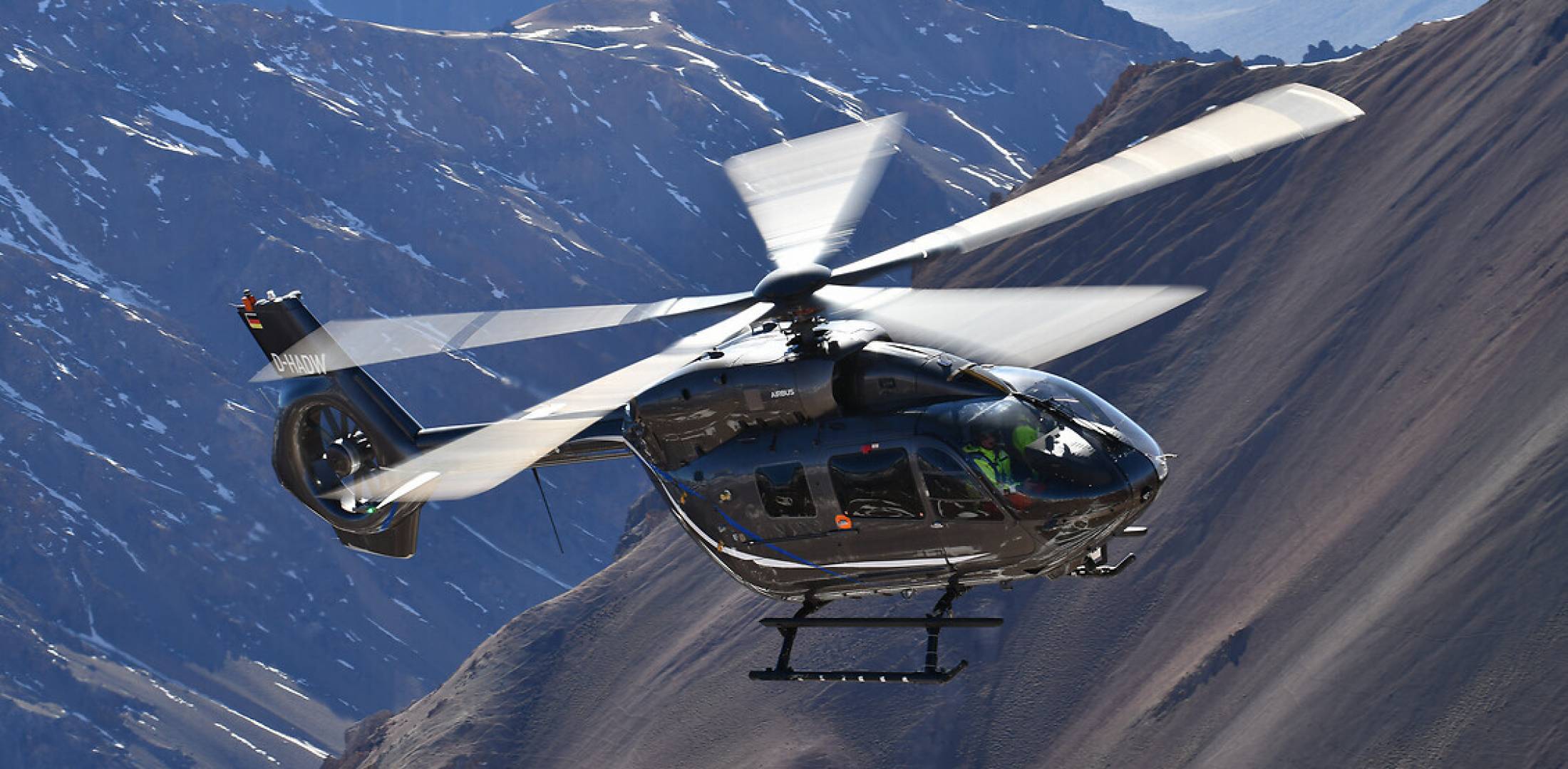 twin-engine H145 helicopter in flight over steep mountainous terrain