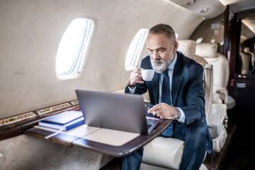 Businessman uses Inmarsat satellite communication to use laptop on business jet